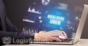 Seorang profesional sedang bekerja di laptop dengan grafik dan teks 'MODEL BISNIS UMKM' muncul pada layar, menunjukkan konsep strategi bisnis untuk Usaha Mikro, Kecil, dan Menengah.